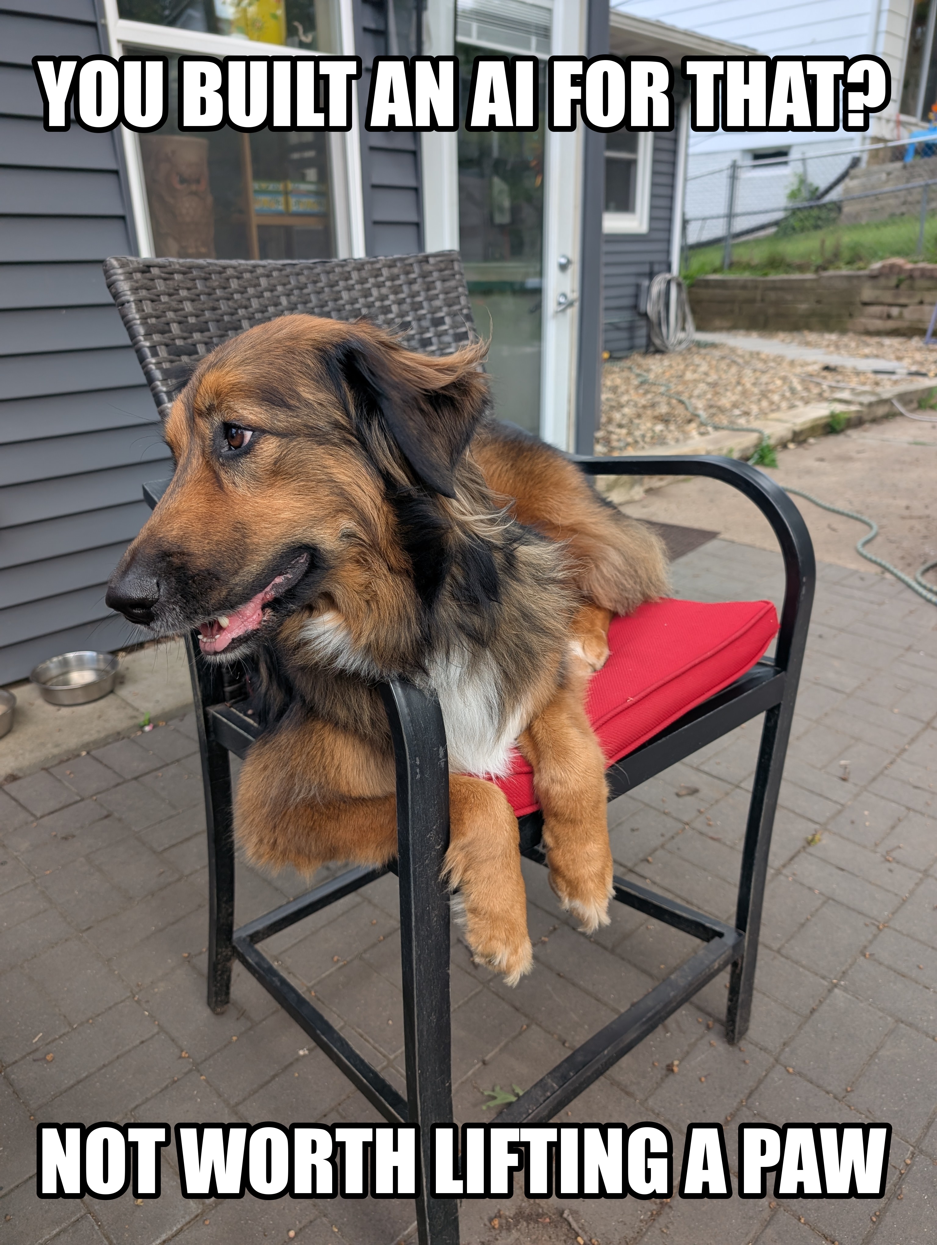 A large brown and black dog draped lazily across a tall black patio bar stool with a red cushion, its front paws dangling off the edge, captioned YOU BUILT AN AI FOR THAT? above and NOT WORTH LIFTING A PAW below